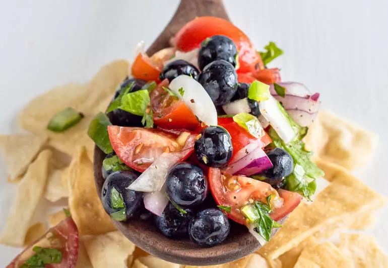 Primo piano della salsa di jalapeno ai mirtilli in un cucchiaio di legno sospeso su tortilla chips.