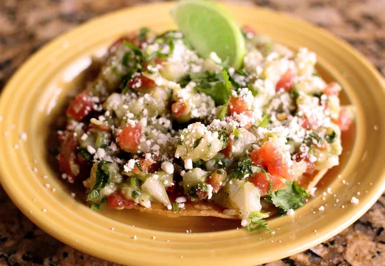 Tostada di pesce su un piatto giallo con pomodori, avocado e lime