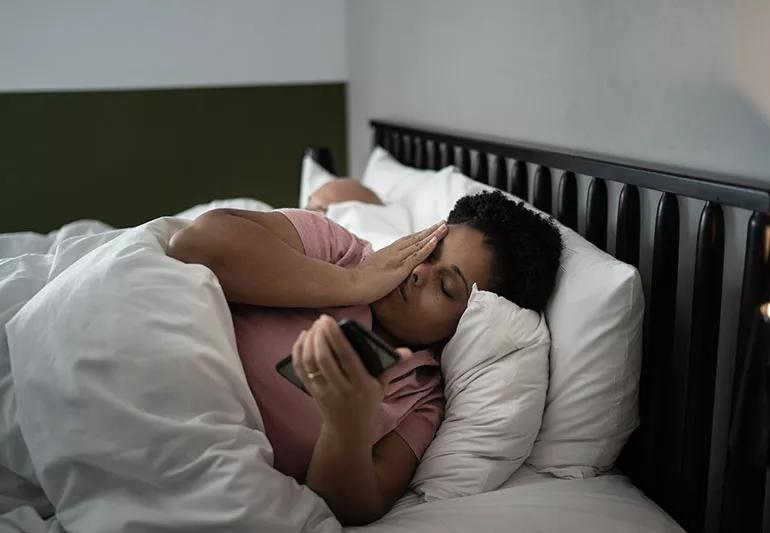 Una persona abbattuta tiene il cellulare in una mano mentre si preme l'altra sul viso per la stanchezza.